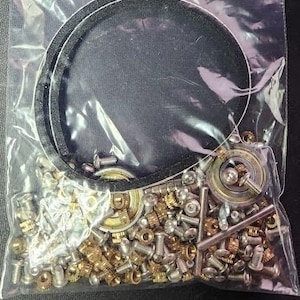 May include: A clear plastic bag filled with a variety of small metal parts, including screws, nuts, washers, and bearings. The bag is also filled with a black rubber ring.
