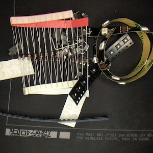 May include: Assortment of electronic components including resistors, LED strips, and a small circuit board. The components are arranged on a black surface. The text on the LED strip reads "200MP" and "100MP". The text on the circuit board reads "45W MAX/ 883.2*323.2mm 02020 BY NOWZRE FOR WIRELESS FUTURE MADE IN CHINA".