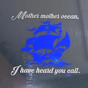 May include: A blue silhouette of a pirate ship with a skull and crossbones on the sail. The text "Mother mother ocean, I have heard you call." is written in white on a black background.