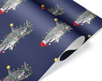 Puede incluir: Papel de regalo con un patrón repetido de tiburones de dibujos animados decorados con luces navideñas y gorros de Papá Noel. Los tiburones son grises con vientres blancos, sobre un fondo azul oscuro. Estrellas amarillas salpican el diseño.