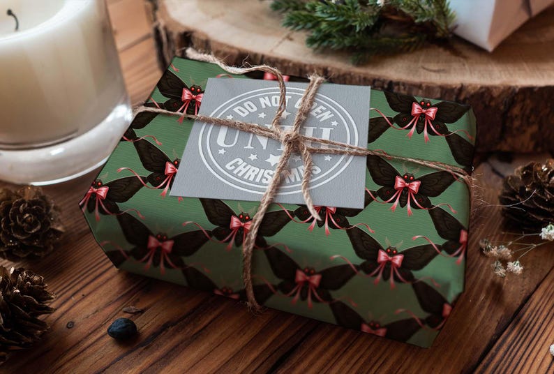 May include: A wrapped gift with green paper featuring a repeating pattern of black moths with pink bows. The gift is tied with twine and has a gray tag that reads "DO NOT OPEN UNTIL CHRISTMAS". The gift is on a wooden surface.