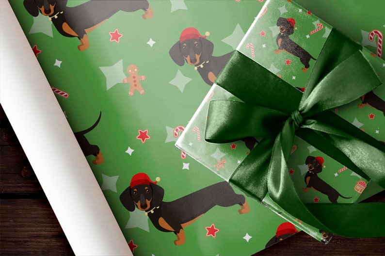 K&ouml;nnte beinhalten: Gr&uuml;nes Geschenkpapier und ein verpacktes Geschenk mit einer dunkelgr&uuml;nen Satinschleife. Das Papier zeigt ein sich wiederholendes Muster aus Dackeln mit Weihnachtsm&uuml;tzen, Sternen, Lebkuchenm&auml;nnern und Zuckerstangen. Das Geschenk ist bereit f&uuml;r die Feiertage.