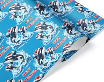 Può includere: Un rotolo di carta da regalo con sfondo blu brillante caratterizzato da un motivo ripetuto di orche bianche e nere che indossano cappelli rossi da Babbo Natale, che saltano fuori da onde blu, con il testo rosso Merry Christmas.