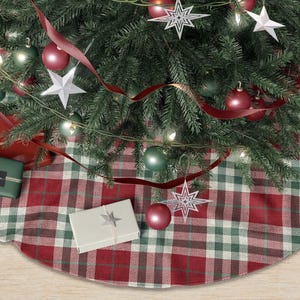 May include: A decorated Christmas tree with red and green ornaments, star-shaped decorations, and a red ribbon. The tree sits on a red, green, and white plaid tree skirt. Several wrapped gifts are at the base of the tree.