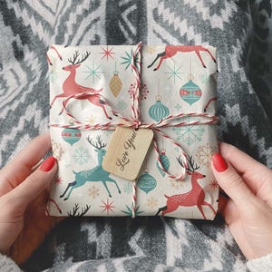 May include: A wrapped gift with a festive pattern featuring red and teal reindeer, ornaments, and snowflakes. The gift is tied with red and white twine and a small tag that says "Love You!"