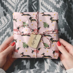 Op de afbeelding: Een roze cadeaudoos verpakt in papier met een teckelpatroon. De doos is vastgebonden met touw en heeft een houten cadeaulabel met de tekst "Love You!"