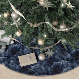 May include: A Christmas tree skirt with a dark blue faux fur design. The skirt is beneath a decorated Christmas tree with ornaments, lights, and ribbon. Several wrapped gifts are placed on the skirt.