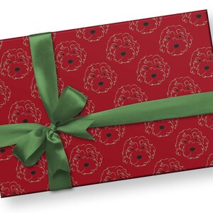 May include: A wrapped gift with red wrapping paper featuring a repeating pattern of dog faces in a light color. A green ribbon is tied around the gift in a bow.