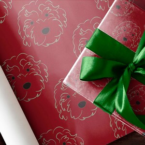 May include: A red gift box with a green satin ribbon bow sits atop red wrapping paper patterned with light green dog faces. A roll of white wrapping paper is visible on the left.