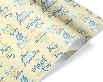 May include: Off-white wrapping paper with a repeating pattern of blue and gold Hanukkah-themed text and illustrations. The design includes phrases like "Happy Hanukkah," "Mazel Tov," and dreidels.