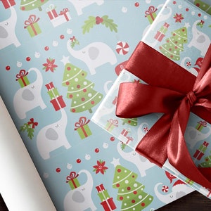 May include: Christmas-themed wrapping paper and a wrapped gift with a red satin bow. The wrapping paper features a light blue background with white elephants, Christmas trees, and gift boxes. The gift box is wrapped in the same paper.