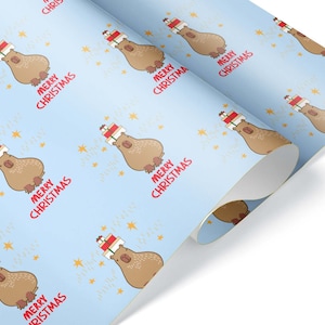 May include: Light blue wrapping paper with a repeating pattern of cartoon capybaras wearing Santa hats and carrying gifts. The words "MERRY CHRISTMAS" are printed in red below each capybara, with gold stars scattered across the background.