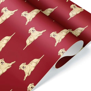 May include: Red wrapping paper featuring a repeating pattern of light tan Labrador Retrievers in a playful pose. The dogs are illustrated with detailed features, set against a solid red background. The paper is partially rolled, revealing a white underside.