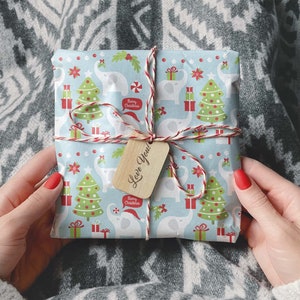 May include: A wrapped gift with a light blue background featuring white elephants, Christmas trees, and gift boxes. The gift is tied with red and white twine and a wooden tag that says "Love You!". The wrapping paper also has the text "Merry Christmas".