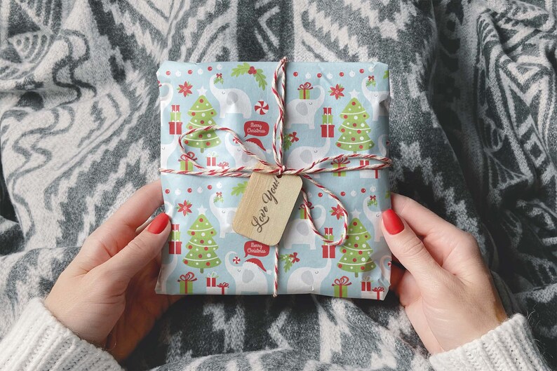 May include: A wrapped gift with a light blue background featuring white elephants, Christmas trees, and gift boxes. The gift is tied with red and white twine and a wooden tag that says "Love You!". The wrapping paper also has the text "Merry Christmas".