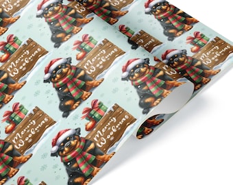 Può includere: Carta da regalo con un motivo ripetuto di un cucciolo di Rottweiler con cappello da Babbo Natale e sciarpa a righe rosse e verdi, accanto a un cartello in legno con il testo Merry Woofmas e un regalo, su sfondo azzurro con fiocchi di neve.