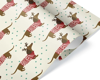 May include: A roll of cream-colored wrapping paper featuring a repeating pattern of dachshunds wearing red sweaters with white patterns and reindeer antlers. The background has small teal dots.