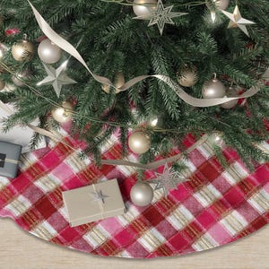 May include: A Christmas tree skirt with a red and pink plaid pattern. The skirt is under a decorated Christmas tree with ornaments, lights, and ribbon. There are wrapped gifts on the skirt.