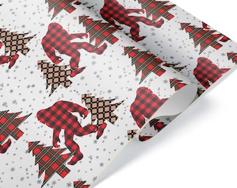 May include: White wrapping paper with a repeating pattern of red and black plaid Bigfoot figures, Christmas trees, and snowflakes. The trees are red and green plaid, and brown and tan diamond patterns. The paper is rolled up in the corner.