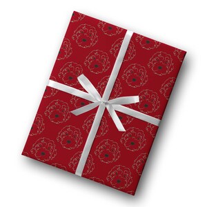 May include: A rectangular gift wrapped in red paper with a repeating pattern of dog faces in gold outlines. A white satin ribbon is tied around the gift in a bow. The gift wrap is a festive design.