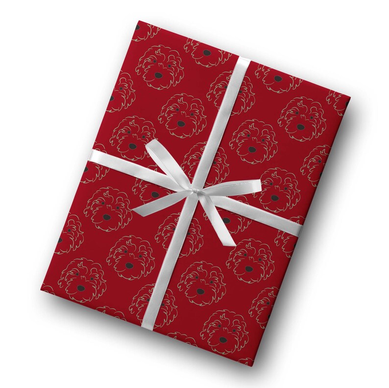 May include: A rectangular gift wrapped in red paper with a repeating pattern of dog faces in gold outlines. A white satin ribbon is tied around the gift in a bow. The gift wrap is a festive design.