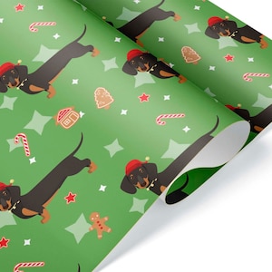 K&ouml;nnte beinhalten: Gr&uuml;nes Geschenkpapier mit einem sich wiederholenden Muster aus Dackeln mit Weihnachtsm&uuml;tzen, Lebkuchenm&auml;nnern, Zuckerstangen, Sternen und Lebkuchenh&auml;usern. Die Dackel sind schwarz und braun mit roten M&uuml;tzen. Der Hintergrund ist gr&uuml;n.