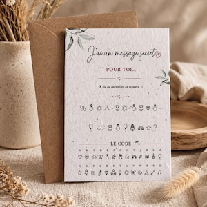 May include: A white rectangular card with a textured surface featuring the French text J'ai un message secret POUR TOI, a series of icon symbols, and a decoding key labeled LE CODE with letters A through Z paired with corresponding small line art icons.