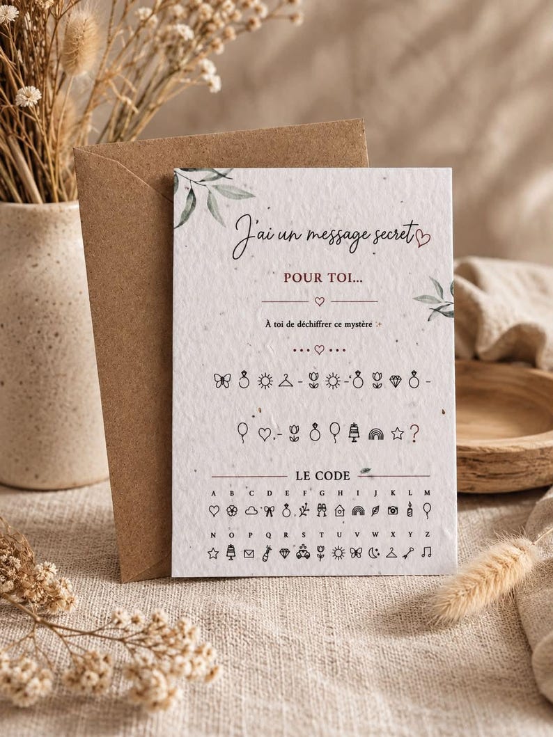May include: A white rectangular card with a textured surface featuring the French text J'ai un message secret POUR TOI, a series of icon symbols, and a decoding key labeled LE CODE with letters A through Z paired with corresponding small line art icons.
