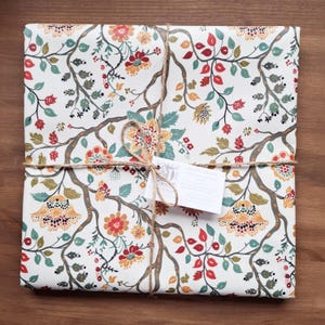 Peut inclure: Un cadeau emballé dans du papier à motifs floraux avec des fleurs rouges, orange et turquoise sur fond blanc. Le paquet est noué avec de la ficelle et une petite étiquette. Sur une surface en bois.