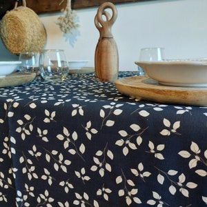 May include: A dark blue tablecloth with a white leaf pattern. The table is set with wooden bowls, clear glasses, and a decorative wooden sculpture. The overall theme is rustic and natural.