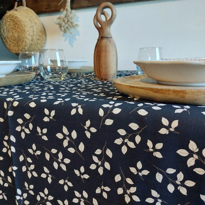 May include: A dark blue tablecloth with a white leaf pattern. The table is set with wooden bowls, clear glasses, and a decorative wooden sculpture. The overall theme is rustic and natural.