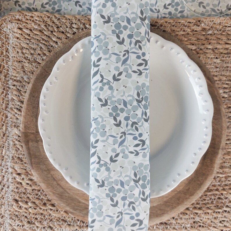 May include: A white ceramic plate with a scalloped edge sits on a wooden charger. A woven placemat is underneath the charger. A blue and white patterned napkin is placed on top of the plate.