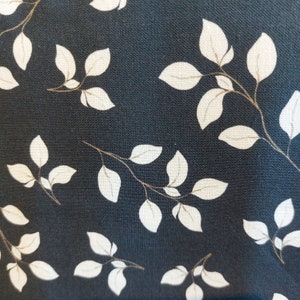 May include: Close-up of fabric featuring a repeating pattern of white leaves and brown stems on a dark blue backdrop. The leaves display detailed veins, creating a natural, botanical theme. The fabric has a textured appearance.