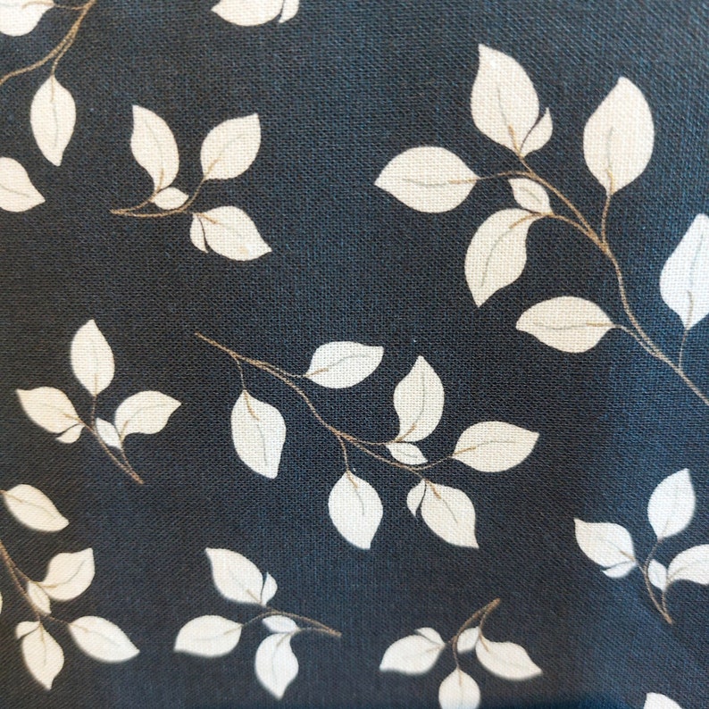 May include: Close-up of fabric featuring a repeating pattern of white leaves and brown stems on a dark blue backdrop. The leaves display detailed veins, creating a natural, botanical theme. The fabric has a textured appearance.