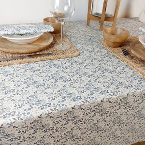 May include: A white tablecloth with a blue and gray floral pattern. The tablecloth is set with a place setting, including a plate, bowl, glass, and silverware.