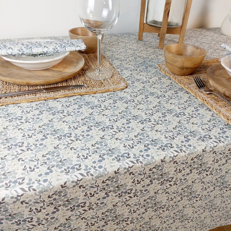 May include: A white tablecloth with a blue and gray floral pattern. The tablecloth is set with a place setting, including a plate, bowl, glass, and silverware.