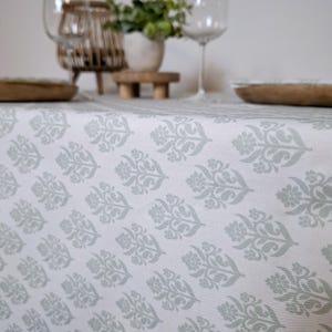 Peut inclure: Nappe blanche avec un motif floral gris répété. La nappe est posée sur une table avec une surface en bois.