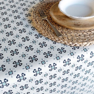 Puede incluir: Un mantel blanco con un patrón geométrico repetitivo en negro y azul. Un plato de madera con un tazón blanco y un tenedor están sobre un mantel individual tejido.