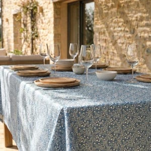 May include: A dining table set for a meal outdoors. The table is covered with a blue tablecloth with a white floral pattern. Wooden plates, bowls, and wine glasses are arranged on the table, creating a rustic and elegant setting.