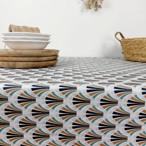 May include: A white tablecloth featuring a repeating fan design in teal, black, brown, and gold. Wooden plates and white bowls are stacked on the table. A woven basket and a roll of twine are also visible.