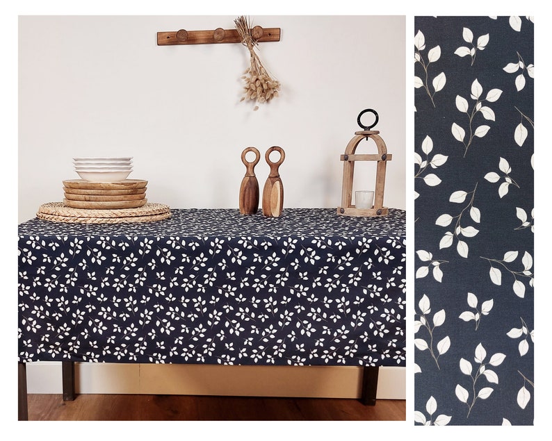 May include: A dark blue tablecloth with a white leaf design. The table is set with white bowls, wooden plates, and a woven placemat. Decorative wooden items and a candle lantern are also on the table.