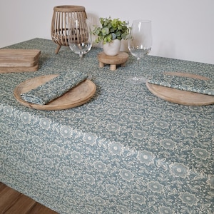 May include: A blue tablecloth with a white floral pattern. The tablecloth is set with two place settings, each with a wooden plate, a napkin, and a wine glass.