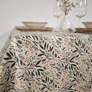 Könnte beinhalten: Eine cremefarbene Tischdecke mit einem botanischen Muster aus grünen Blättern, roten Beeren und braunen und gelben Akzenten. Die Tischdecke bedeckt einen Tisch, der mit Tellern, Schalen und Gläsern gedeckt ist und eine rustikale, natürliche Ästhetik erzeugt.
