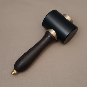 May include: A black leather mallet with a dark wood handle and brass accents. The mallet is used for leatherworking and crafting.