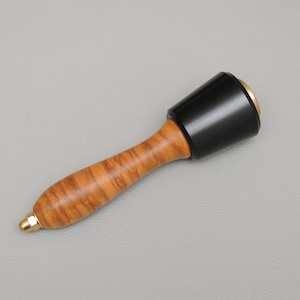 May include: A wooden mallet with a black rubber head and gold accents. The handle is made of wood with a natural grain pattern.