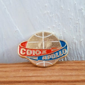 May include: A gold-colored pin with a globe design and a red and blue ribbon around it. The ribbon says "СОЮЗ АПОЛЛО" in Cyrillic and Latin script.
