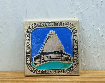 Puede incluir: Un pin de esmalte plateado y azul con una imagen estilizada de una casa tradicional ucraniana con el texto "Музей народної архітектури та побуту Української РСР" (Museo de Arquitectura Popular y Vida Cotidiana de la RSS de Ucrania).