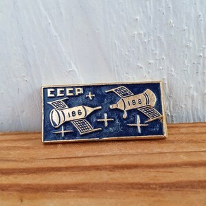 May include: A blue and gold enamel pin with the text "CCCP" and two spacecrafts with the numbers "186" and "188".