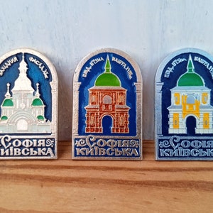 Może przedstawiać: Trzy srebrne metalowe szpilki z niebieską, zieloną i żółtą emalią. Każda szpilka przedstawia inny detal architektoniczny Soboru Świętej Sofii w Kijowie na Ukrainie. Na każdej szpilce widnieje napis "Софія Київська".