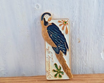 May include: A white enamel pin with a gold-colored bird and green and gold floral design. The pin says "Веселый  Праздник" in gold lettering.